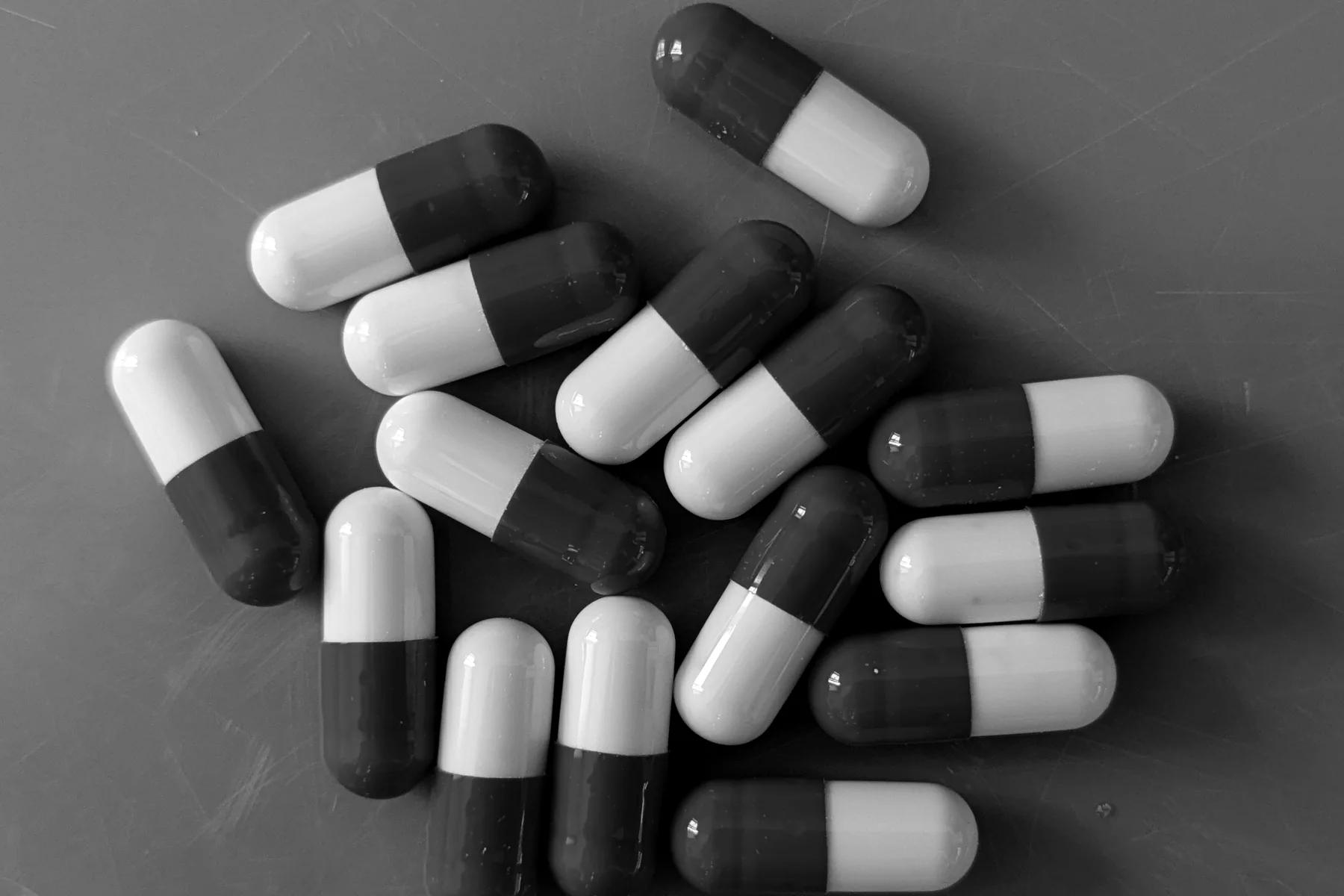 A pile of two-tone capsules on a grey surface, in black and white